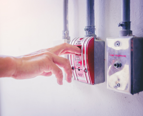 Man’s hand pulling fire alarm switch on the wall at the fire exit door in factory